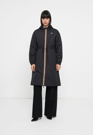 Black hooded raincoat with a yellow and red zipper, cinched waist, and elastic cuffs. Styled with wide-legged black pants.