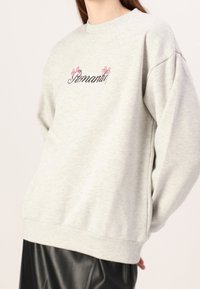 Maglione grigio realizzato in morbido tessuto, con maniche raglan e testo ricamato con fiocchi rosa, ha una vestibilità rilassata e polsini a coste.
