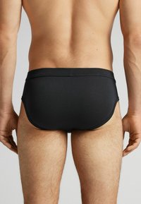 Zwarte zwemboxers met een gladde textuur, elastische tailleband en een strakke pasvorm. Kenmerkt zich door minimale stiksels en een klassieke snit.