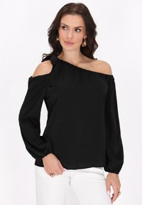 Musta off-the-shoulder-paitapusero, jossa on pitkät puffihihat, kevyestä kankaasta valmistettu, sisältää solmukoristeen yhdellä olalla ja elastisen helman.