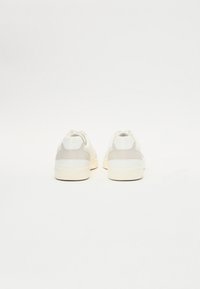 Weiße und hellgraue Sneakers mit einer glatten Leder- und Wildleder-Oberfläche, ausgestattet mit einer abgerundeten Spitze und einem minimalistischen Design.