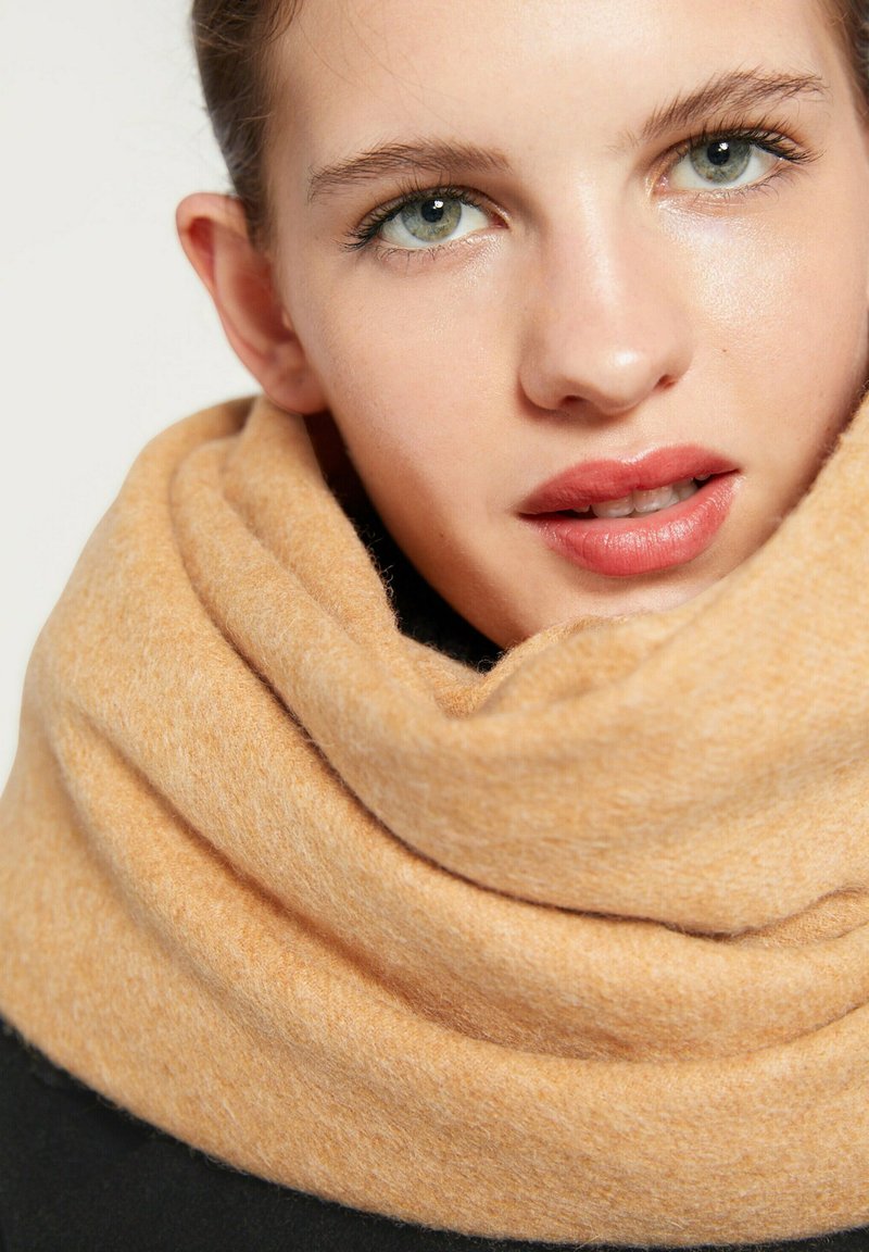 Écharpe douce, orange pâle en laine, présentant une texture épaisse et confortable, drapée en une boucle continue autour du cou.