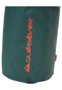 Bolsa seca impermeable verde, fabricada con material duradero, presenta un logotipo naranja prominente y una superficie texturizada. Base redondeada con un fondo plano.