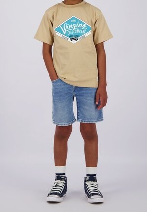 T-shirt en coton beige avec un motif graphique bleu, assorti à un short en denim bleu et des baskets montantes bleu marine avec des lacets blancs et des chaussettes blanches.