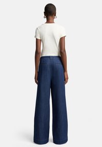 Bredde denim bukser i dyp blå med høy midje; kombinert med en kortermet kremfarget topp som fremhever minimalistisk design og rene linjer.