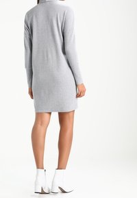 Ljust grått stickat klänning med långa ärmar, helst krage och rak skärning. Kombineras med vita ankelskornor med blockklack.