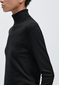 Czarny sweter z golfem wykonany z miękkiej, teksturowanej tkaniny, z długimi rękawami i dopasowanym krojem. Wysoki, prążkowany kołnierz.