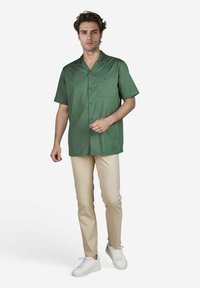 Groene kurzarm shirt met een kraag, een borstzak en knopen. Gecombineerd met beige slim-fit broeken en witte sneakers.