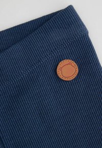 Granatowy żebrowany materiał o teksturowanej powierzchni i brązowa okrągła skórzana naszywka z haftowanym wzorem niedźwiedzia, przyszyta do pasa.