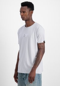 Gaiši pelēks īsām piedurknēm t-krekls ar apaļu kakla izgriezumu un mazu izšūtu uzpleču uz krūtīm. Mīksta tekstūra, ikdienišķs griezums un neliela stiepšanās.