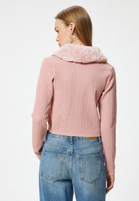 Rosa gestreifter, gestrickter, cropped Pullover mit einem flauschigen Kragen, kombiniert mit hellblauen, hochgeschnittenen Jeans. Das Design hat lange Ärmel und einen strukturierten Stoff.
