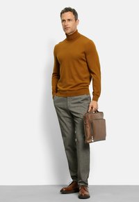 Brauner Rollkragenpullover, graue karierten Hose, braune Lederschuhe und eine braune Aktentasche mit einem Reißverschlussfach. Einfarbiger Hintergrund.
