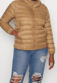 Hnědá prošívaná bunda s vodorovným prošíváním, zipem a kapucí. Kombinována s modrými džínami s výraznými roztrženími na kolenou.