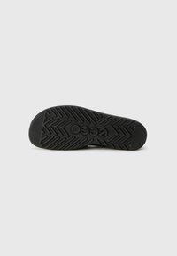 Talpă din cauciuc negru cu un model texturat cu un tipar în zigzag și logo-ul mărcii imprimat în centru.
