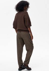 Bruine gebreide trui met een relaxte pasvorm en korte mouwen, gecombineerd met bruine getailleerde tapered broek en zwarte chunky schoenen.