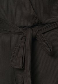 Czarna żebrowana tkanina z wstążką w talii. Tkanina ma teksturowany wzór i gładkie wykończenie. Dodatki obejmują zawiązany kokardę.