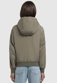 Veste matelassée vert olive avec capuche, poignets et ourlets côtelés. Tissu lisse et brillant avec une coupe légèrement plus ample ; la vue de dos montre les coutures des épaules.