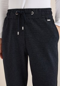 Pantalon de survêtement bleu marine en tissu texturé, avec une ceinture élastique à cordon de serrage et des accents de quincaillerie argentée.