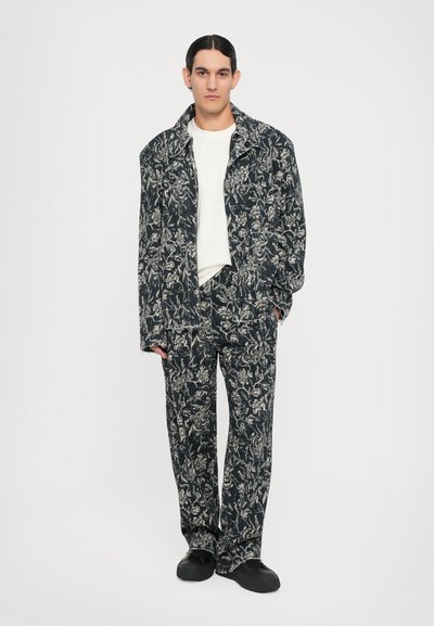 Compleu format din două piese, cu o jachetă bleu închis și pantaloni cu un model floral alb. Materialul pare texturat, cu o croială lejeră și guler.