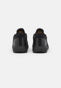 Schwarze Sportschuhe mit einem strukturierten Stoffoberteil, glatten schwarzen Akzenten und einer gemusterten Gummisohle mit einer Zuglasche an der Ferse.