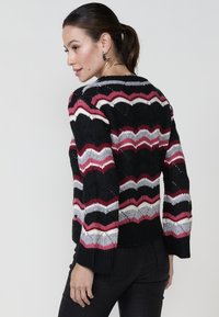 Pull en maille rayé noir, rouge et gris avec un motif en vagues, manches longues et poignets côtelés. Présente un col rond et un dos ouvert.