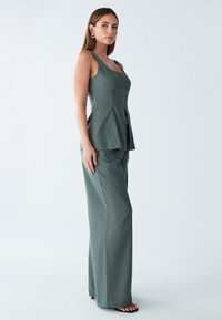 Groen op maat gemaakt set bestaande uit een nauwsluitend mouwloos topje met een vierkante halslijn en broek met wijde pijpen. Gladde textuur, minimalistisch ontwerp en geen zichtbare patronen.