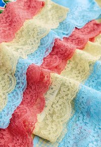 Bandes de tissu en dentelle superposées en bleu pastel, crème et rose avec des motifs floraux et des bords festonnés, disposées en rangées chevauchantes.