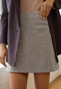 Grau kariertes Rock mit leichter Textur, verfügt über zwei Fronttaschen, eine sitzende Taille und einen ausgestellten Saum, kombiniert mit einem dunklen Blazer.