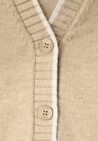 Beżowy sweter z dzianiny z dekoltem w serek, żebrowanymi brzegami i jednym dużym guzikiem. Miękka faktura, prosty design i jasny kolor.