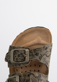 Sandalia de plantilla de corcho con una correa estampada en verde, hebilla ajustable y superficie texturizada. Diseño destalonado con detalles perforados.