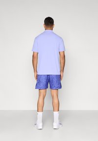 Φωτεινό μωβ πόλο μπλουζάκι σε συνδυασμό με σορτς σε αποχρώσεις του μπλε. Άσπρες κάλτσες και αθλητικά παπούτσια ολοκληρώνουν την εμφάνιση. Καθαρός, casual σχεδιασμός.