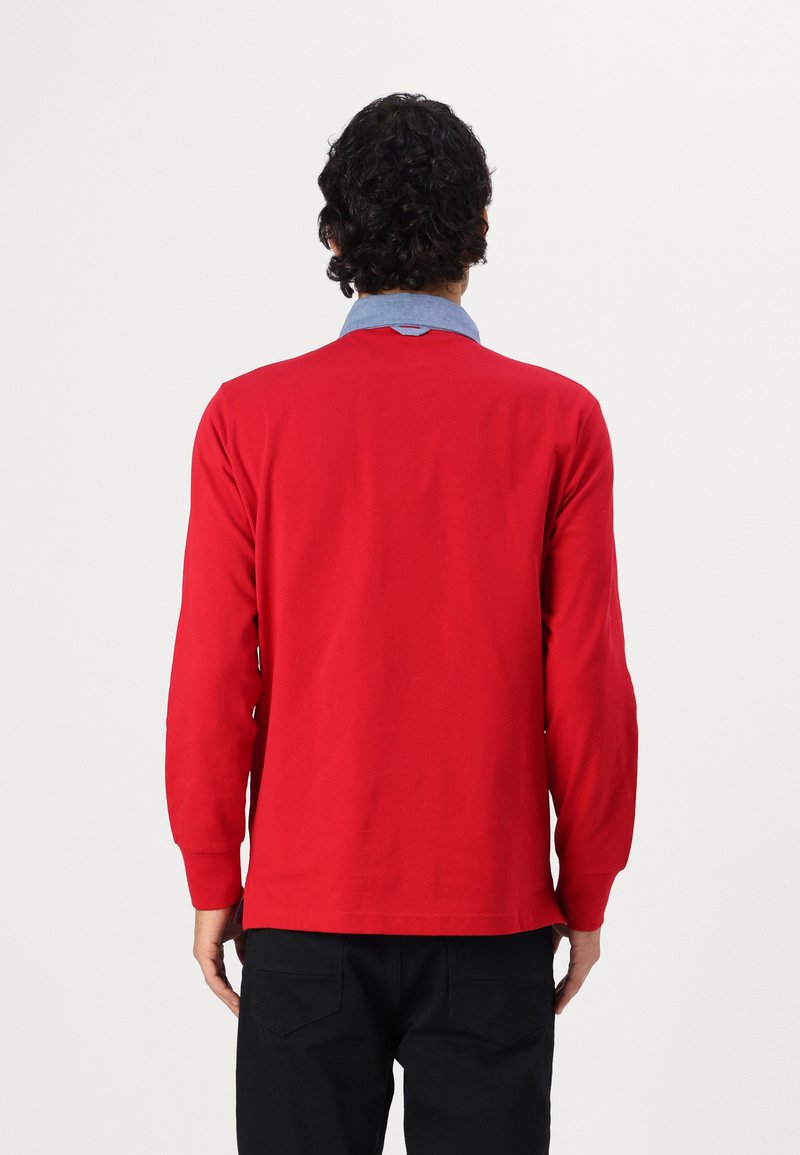 Rotes Langarmshirt mit hellblauem Kragen, weicher Textur und entspannter Passform, Ansicht von hinten. Schwarze Hose nicht sichtbar.