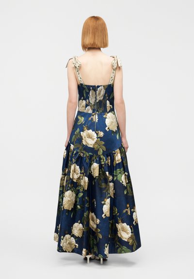 Φλοράλ μάξι φόρεμα σε ναυτικό μπλε ύφασμα, διακοσμημένο με λευκά τριαντάφυλλα και πράσινα φύλλα. Ρυθμιζόμενα φιόγκια στους ώμους και εφαρμοστό μπούστο με φουσκωτή φούστα.