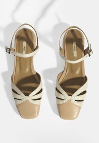 Beige en crème leren sandalen hebben een vierkante neus, een dunne verstelbare enkelband en een uitsnijdingen ontwerp aan de zijkanten voor ventilatie.