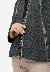 Mörkblå fleecejacka med en texturerad design, dragkedja fram och dragsnören. Har märkesdetaljer och en tight passform vid handlederna.