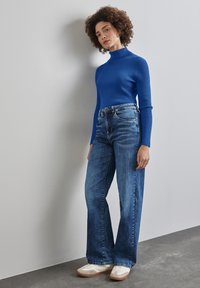 Blå ribbad polotröja med långa ärmar, parat med vida, blekblå jeans och vita sneakers med beige detaljer.