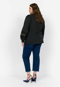 Svart blus med spetsdetaljer på puffärmarna, i kombination med blå cropped jeans och blå högklackade skor. Enkel, kroppsnära design.