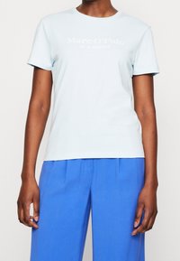 Camiseta de algodón azul claro con mangas cortas y cuello redondeado, con un logo impreso en blanco "Marc O'Polo" en la parte frontal.