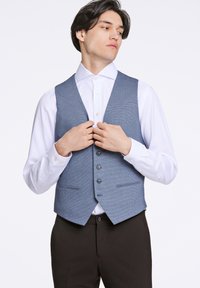 Blå rutigt väst av texturerat tyg. Har fem knappar, två framfickor och en notchkrage, bärs över en vit skjorta.