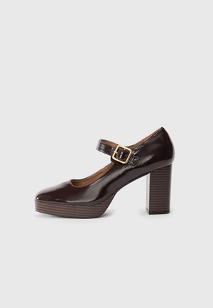 Brown patent leather Mary Jane shoes with a chunky square heel, buckle strap closure, and a textured wooden platform.