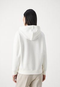 Felpa bianca con cappuccio realizzata in tessuto morbido, dotata di un cappuccio con cordino, polsi e orlo a coste. Il design è semplice e privo di decorazioni, adatto per essere indossato a strati.