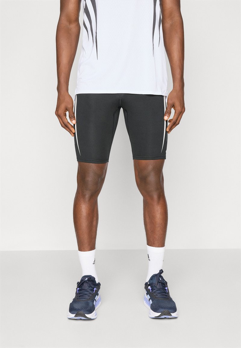 Pantaloni sportivi neri con strisce bianche sui lati, abbinati a una camicia bianca a fantasia, calzini bianchi e scarpe da corsa blu navy.