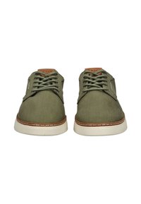 Zapatos de lona verde oliva con cordones a juego, suelas de goma crema y detalles en cuero marrón en el talón y la lengua.