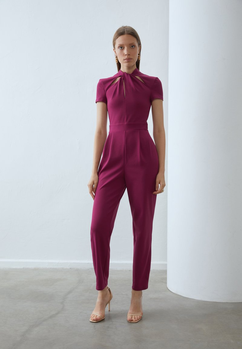 Aansluitende mijngemaakte jumpsuit in magenta met korte mouwen, open halslijn en taille detail. Glad materiaal met een verzorgde silhouet en taps toelopende benen.