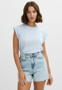 Camiseta de algodón azul claro con mangas enrolladas, combinada con pantalones cortos de mezclilla claros de tiro alto con dobladillo deshilachado y un ligero desgaste.