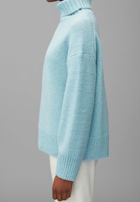 Jasnoniebieski sweter w formie golfu o luźnym kroju, z prążkowanymi mankietami i teksturowanym wzorem dzianiny. Miękki, przytulny materiał zaprojektowany z myślą o komforcie.