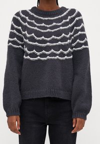 Gruby sweter dzianinowy w ciemnoszarym kolorze z białymi falistymi paskami na klatce piersiowej. Posiada prążkowany dekolt oraz rękawy w stylu balonowym.