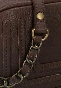 Bolso de cuero texturizado marrón oscuro con detalles cosidos, un remache de latón y una correa de cadena de metal entrelazada con cuero.