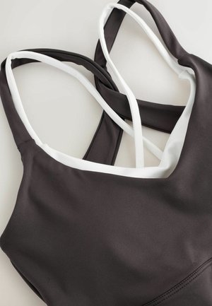 Dunkelgrauer Sport-BH mit weißen Akzenten, ausgestattet mit einem V-Ausschnitt und gekreuzten verstellbaren Trägern. Glatte Textur, für Komfort entworfen.