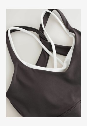 Donkergrijze sportbeha met witte accenten, met een v-hals ontwerp en gekruiste verstelbare bandjes. Glad oppervlak, ontworpen voor comfort.